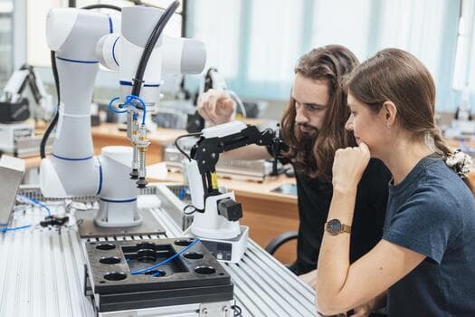 Two students studying a robotic arm on a lab bench